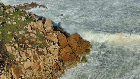 foamy sea waves breaking on rocky cliff in carballo, a coruña, spain - aerial shot