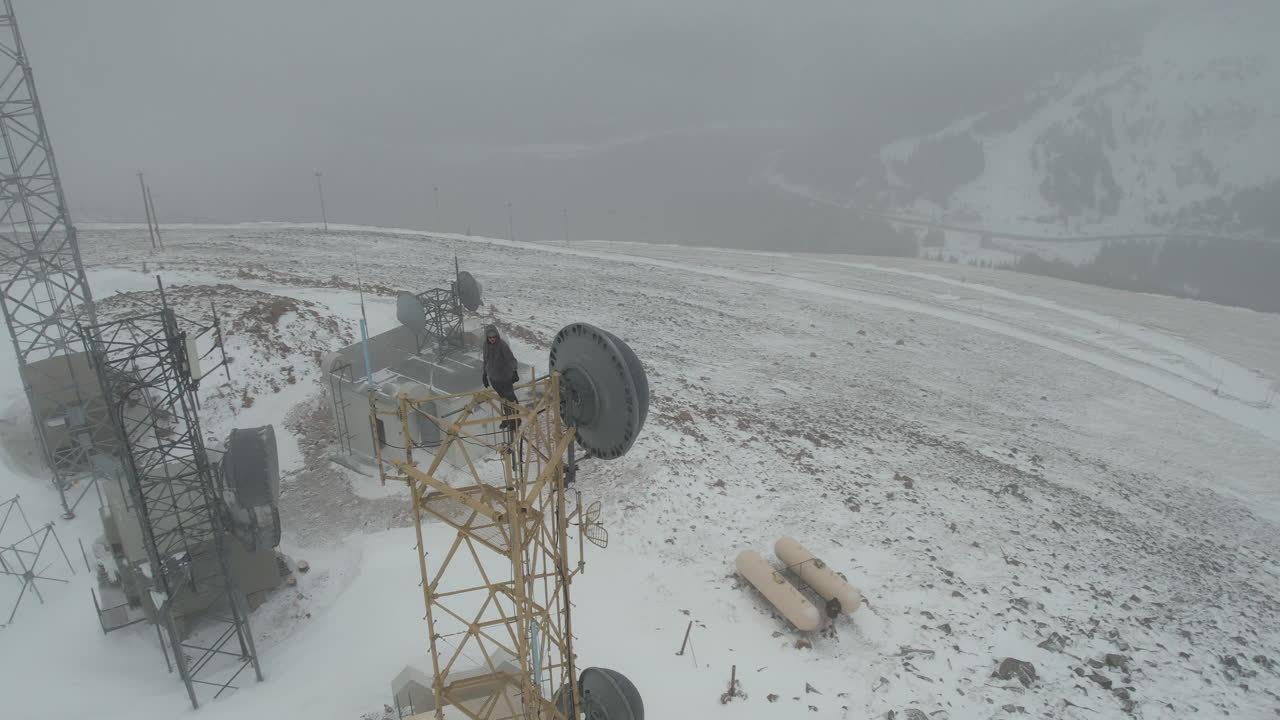 눈 덮인 산 정상에서 안개 속에서 셀 타워 꼭대기에 있는 외로운 남자, 드론 공중 전망