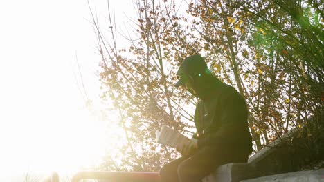 Reader-reading-a-book-while-sitting-on-a-ledge-in-a-park-at-golden-hour---steady-shot