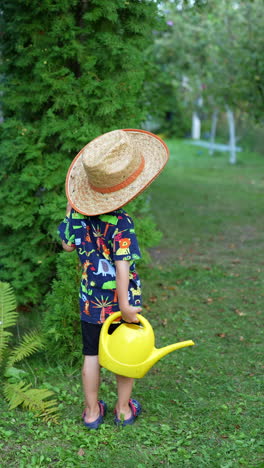 rear view of a little kid splashing water from his yellow watering can. kid in a big straw hat watering the garden. vertical video.