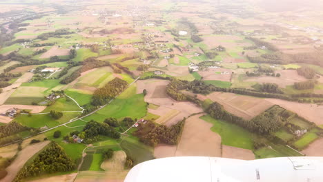 aerial view of the lush countryside from an airplane window, showcasing the patchwork of fields and farmlands