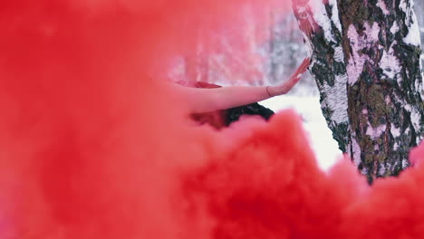 woman in phoenix suit with wings leans on tree in red smoke