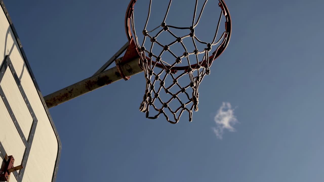 Inquadratura dal basso di un canestro da basket contro un cielo azzurro limpido, che cattura l'essenza dell'aria aperta.