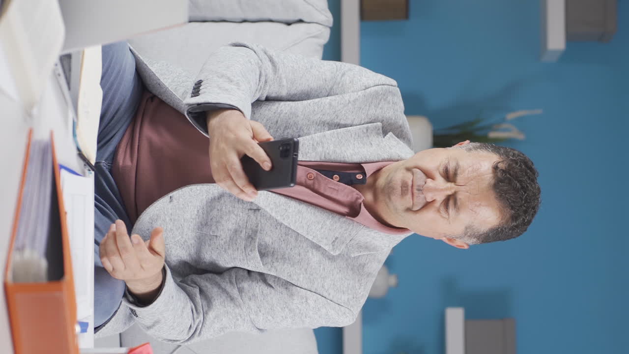 홈 오피스 직원의 수직 비디오  ⁇ 은이가 전화를 보면서 좌절합니다.