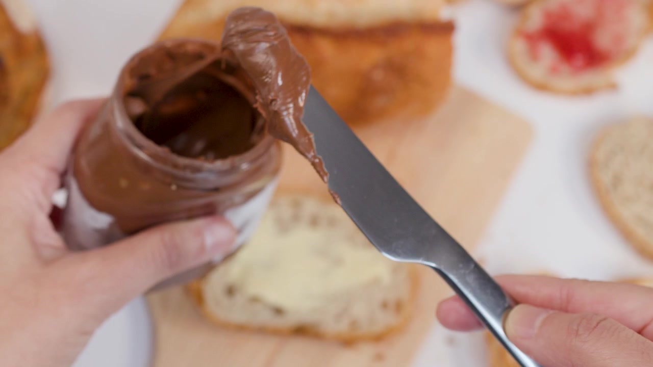 Vista dall'alto di mani che usano un coltello per spalmare crema al cioccolato su pane croccante