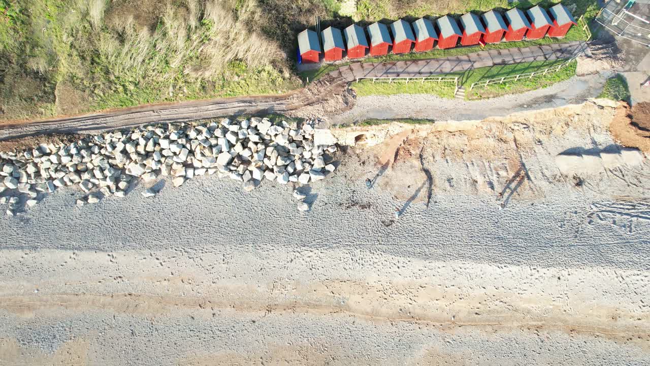 Aerial decending shot of Beach Huts and shingle beach with people walking on the beach, filmed at Branscombe Devon England