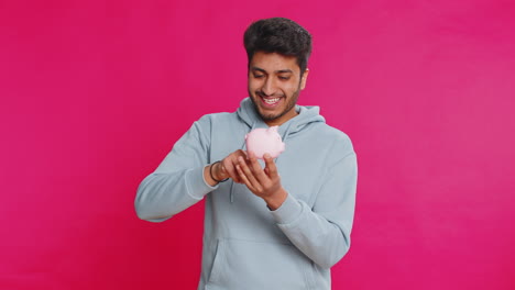 happy indian man holding piggy bank saving money dropping coins planning future financial security