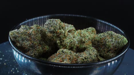 green dried marijuana buds close up concept shot, pile of dried marijuana plants, orange trichomes strains, in small black shiny bawl, on a rotating stand, studio lights, slow motion, 4k video