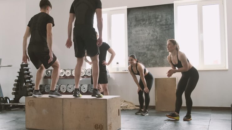 Due giovani uomini che saltano i box mentre i loro compagni di palestra li supportano.