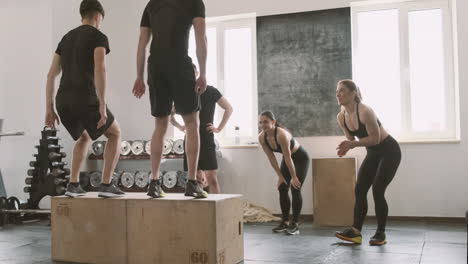 Two-Young-Men-Jumping-The-Boxes-While-Their-Gym-Buddies-Support-Them