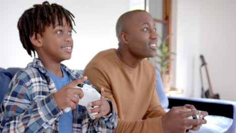 Happy-african-american-father-and-son-playing-video-games-and-fooling-around-at-home,-slow-motion