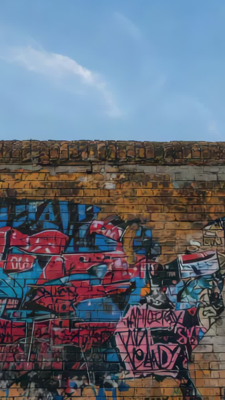 Video verticale: bagliore arancione che si diffonde su un muro con graffiti in un vicolo, rivelando il contrasto