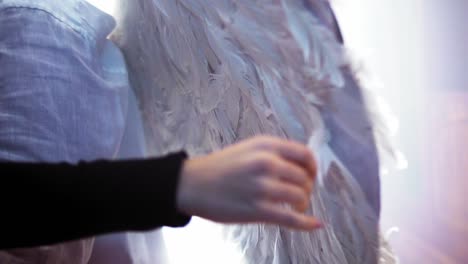 cinematic slow motion shot of a person with feathered wings and a woman touching the feathers with her hand