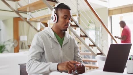 Hijo-Adolescente-Afroamericano-Usando-Audífonos-Usando-Una-Computadora-Portátil-Con-Su-Padre-En-Segundo-Plano