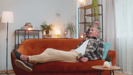 tired young adult man sitting on comfortable couch taking a rest daytime nap resting at home room