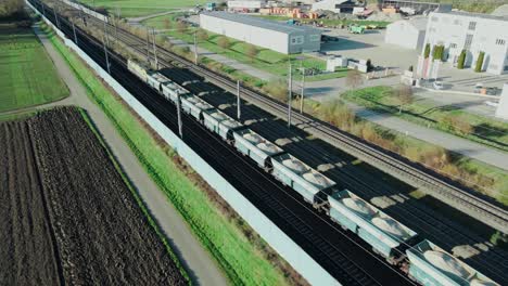 un tren de mercancías que transporta grava a través de una zona industrial es seguido por un dron que vuela junto a las vías del tren