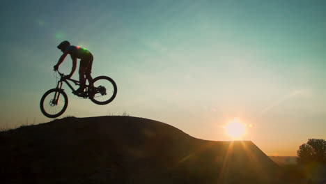 man on mountain bike launches over a dirt ramp in a bike park into the sky