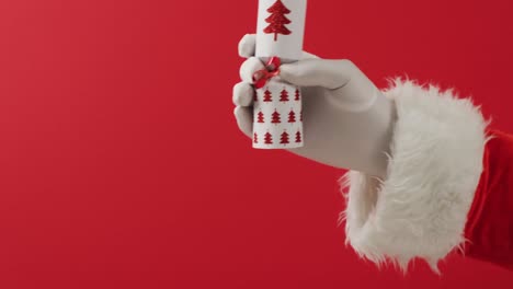 Santa-claus-holding-out-his-hand-with-a-gift-over-red-background