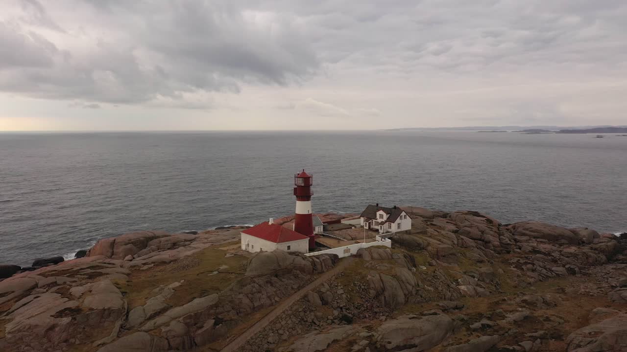 маяк ривинген на закате - красно-белый маяк на маленьком острове в самой южной точке норвегии - аэрофотосъемка на фоне северного моря и драматического неба