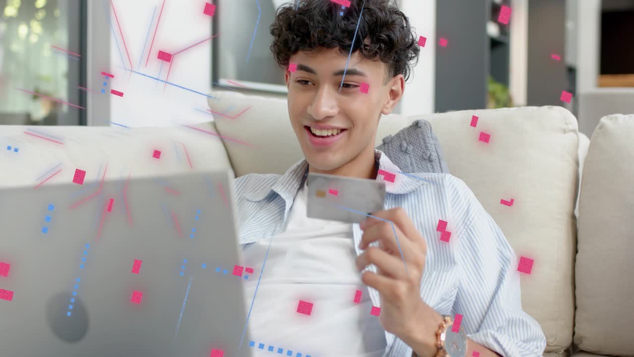 Man on couch holding card and checking laptop, causing animated confetti confirming fintech payment