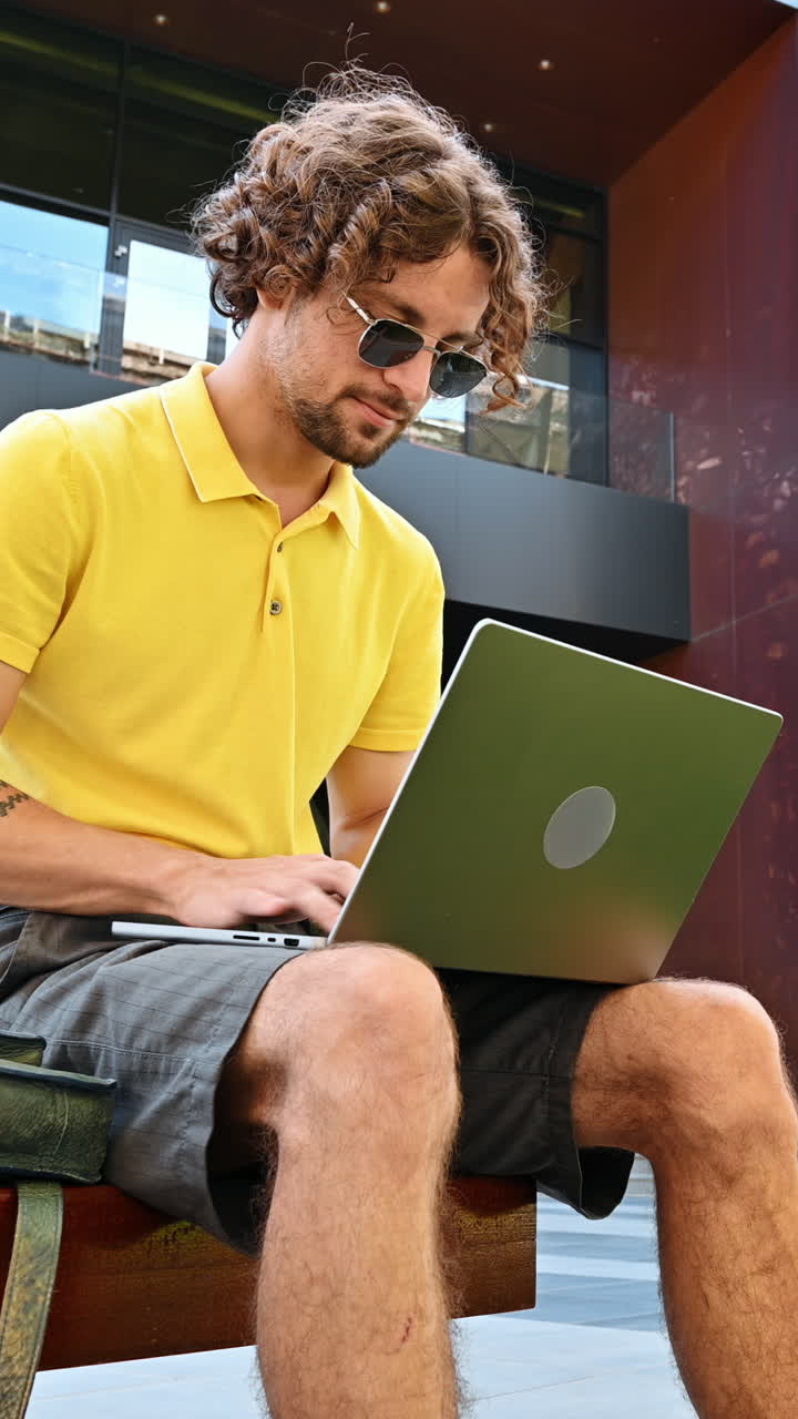 Man in yellow shirt talking standing on a bench and working on a laptop. Vertical
