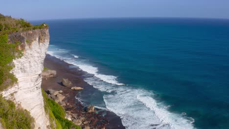 Majestic-cliff-standing-tall-beside-coastline-of-beach-and-low-tides-moving-towards-them