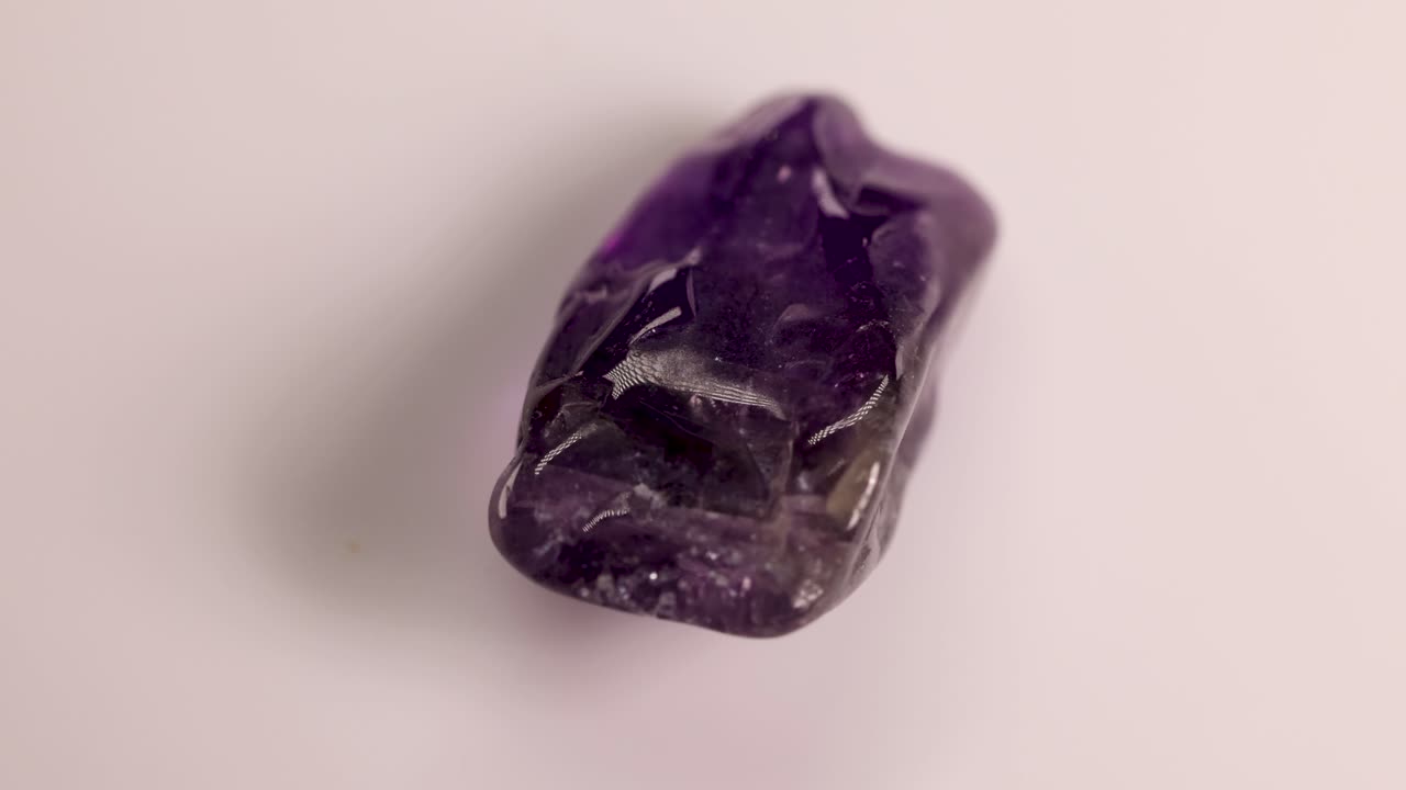 A single amethyst stone rotates on a white surface, showcasing its facets and deep purple hues under soft lighting