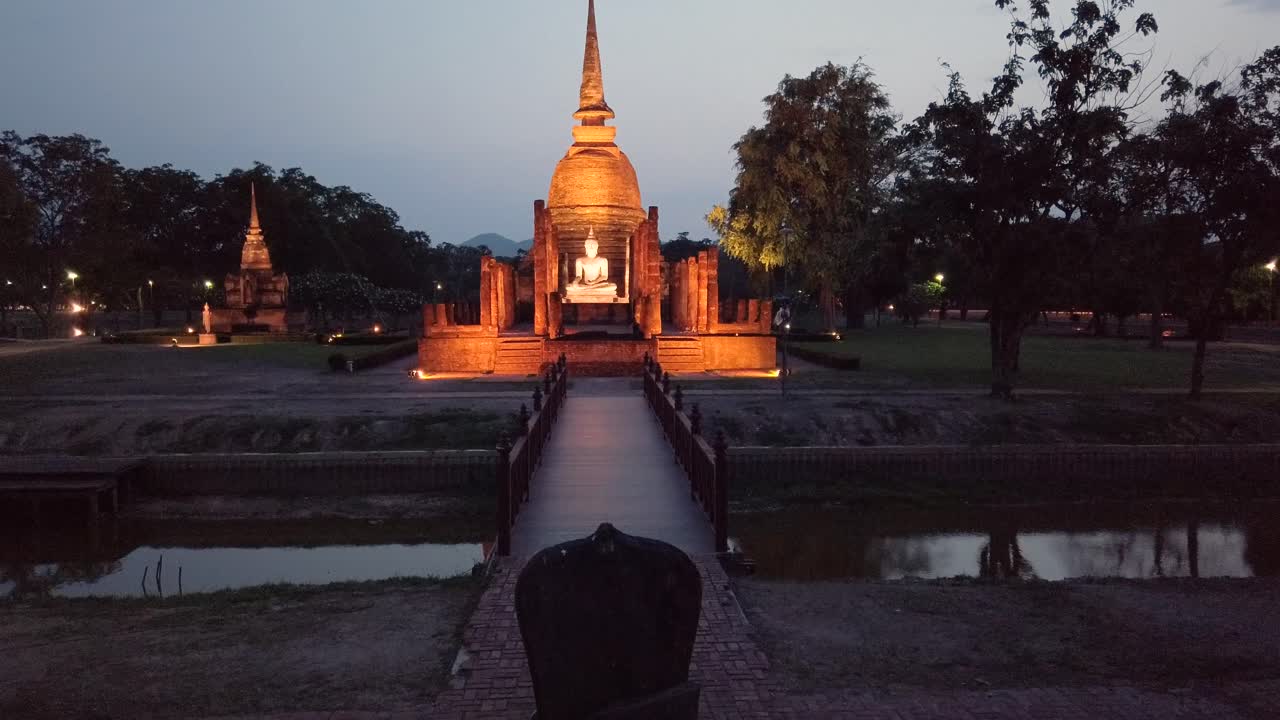 estatua del parque histórico de sukhothai iluminada bajo un cielo estrellado resplandor misterioso con una silla de piedra para sentarse frente al templo del señor buddha