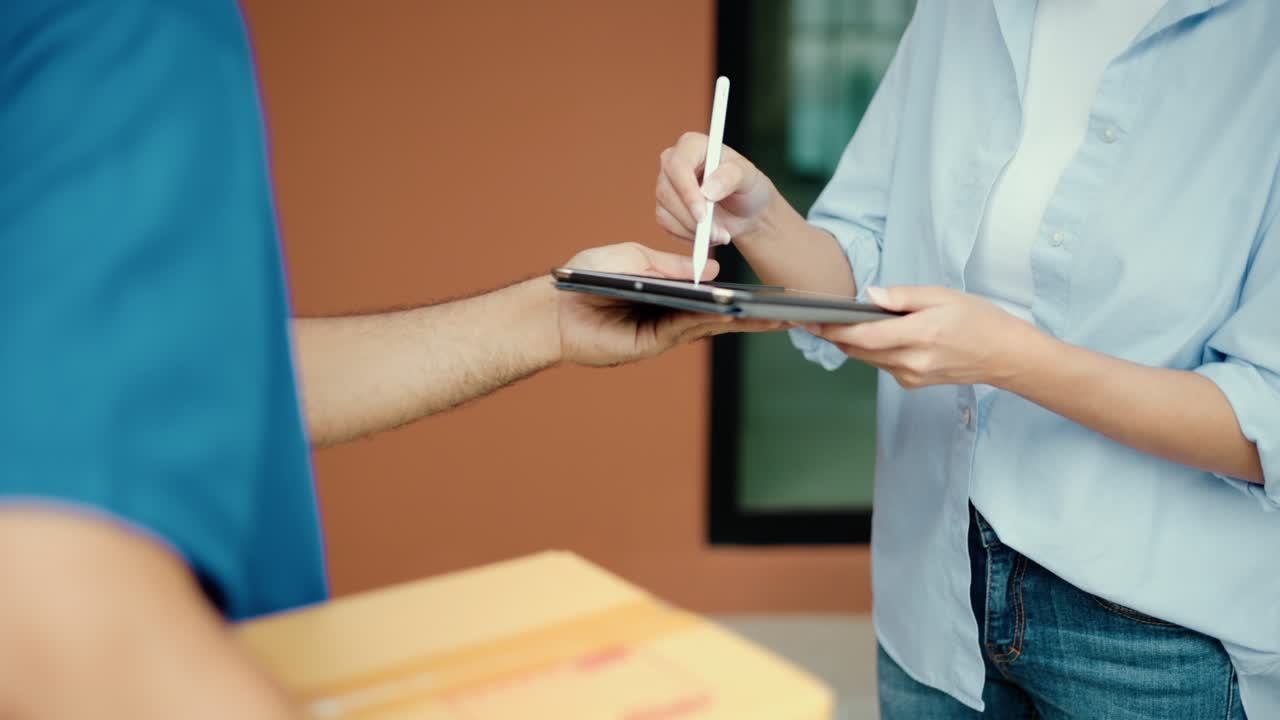 mujer de mano firmando firma electrónica en la tableta para el acuerdo del contrato digital recibiendo el paquete del hombre de entrega azul de las compras en línea. mensajero hombre entregando el paquete al destino.
