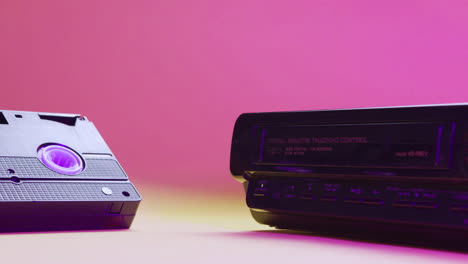 Close-up-view-of-video-VHS-device-and-cassette-on-pink-background