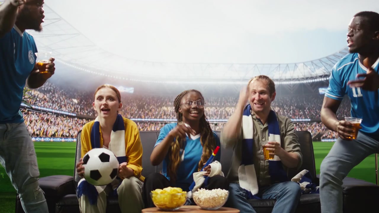 Aficionados al fútbol celebran un gol en casa, viendo una transmisión inmersiva.
