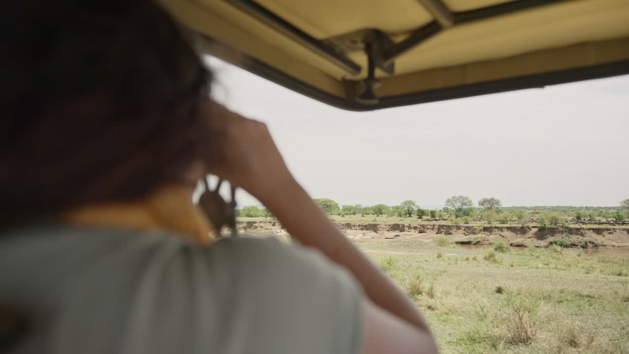 Woman in safari tour looking outside while on game drive pointing at animals. Enjoying vacation in Africa female tourist or explorer traveling in 4x4 special open roof truck watching wild animals