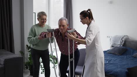 anciano con muletas dando sus primeros pasos con el apoyo de su esposa y el médico