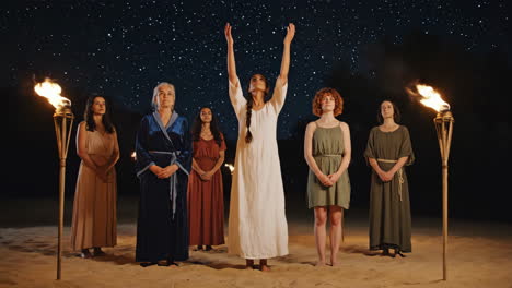 group of women performing a ritual under a starry night sky with torches