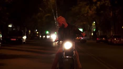 Bearded-rider-sitting-on-a-motocycle,-turning-higly-bright-the-headlight-standing-on-the-night-city-street
