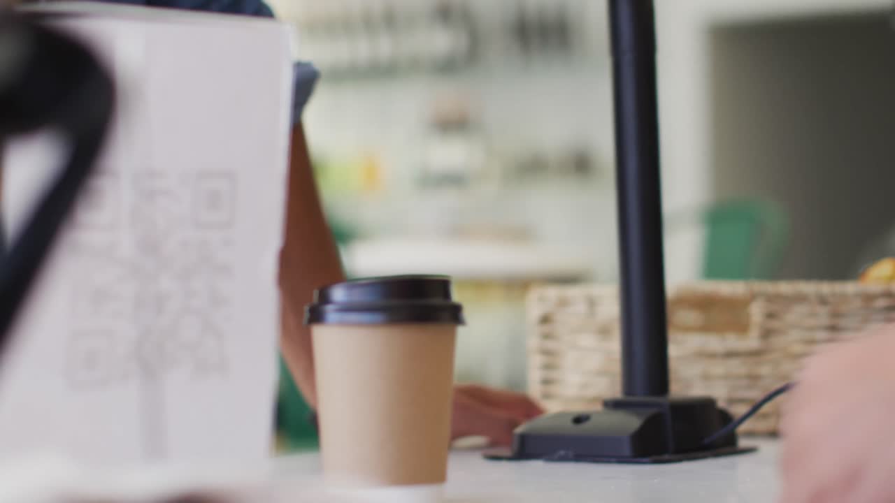 Video delle mani di una cameriera di etnia mista che serve il caffè e tiene in mano un terminale di pagamento.