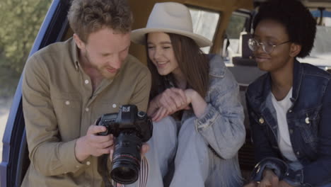 a young photographer shows the pictures he has taken to two beautiful young girls inside the caravan during a roadtrip 2