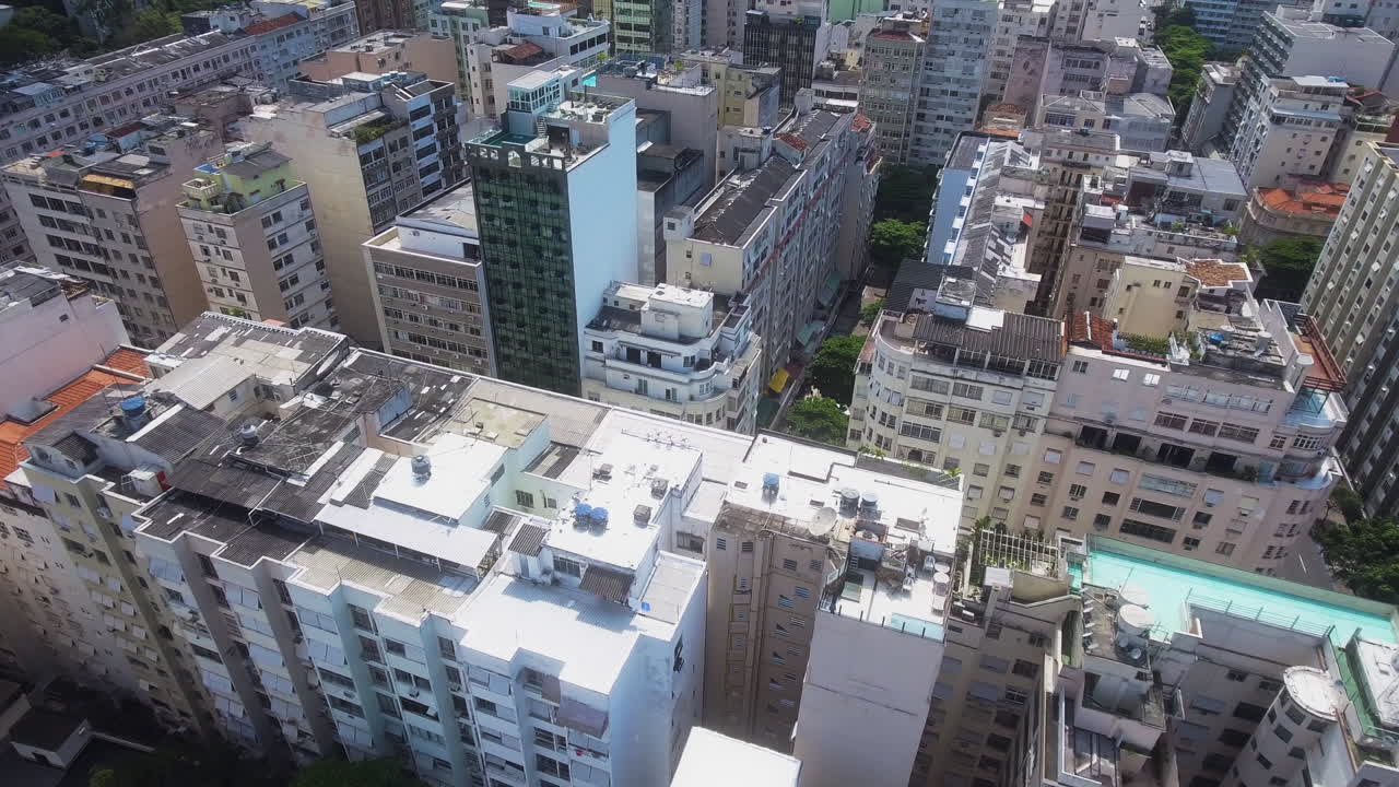 Drone se afasta e eleva, revelando um bairro denso do Rio