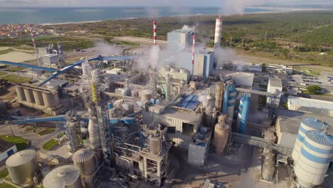 Aerial-close-orbit-over-the-big-industrial-plant-on-a-sunny-day---bird's-eye-view-of-a-modern-cellulose-factory-with-an-ocean-behind