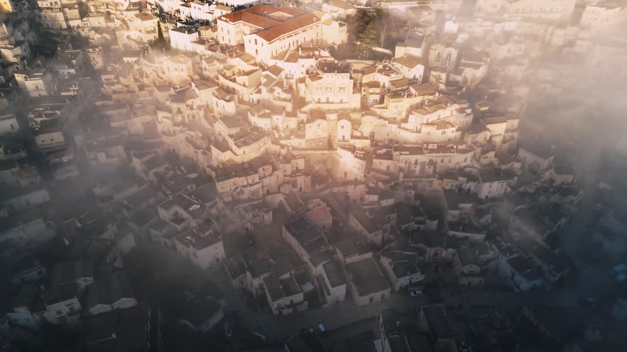 drone shot of old Italian city town - Matera. The city is shrouded with low handing clouds, buildings are visible through them. Warm colours of the rising sun reflected against buildings