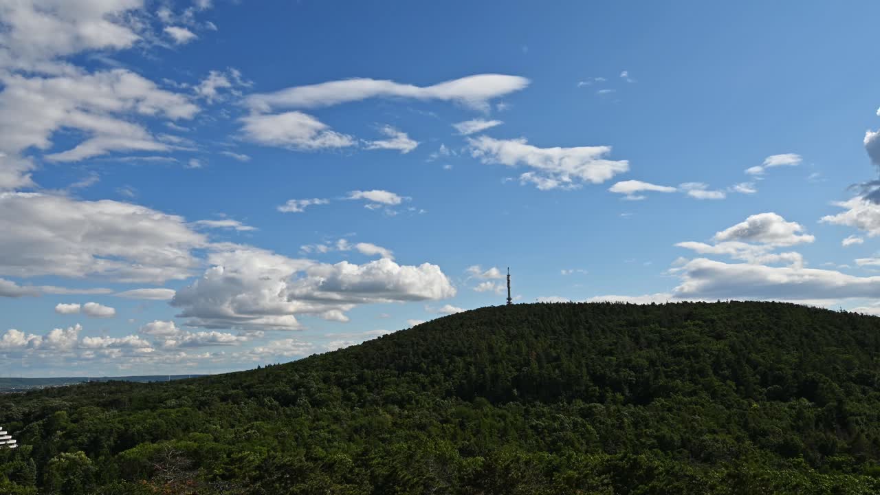 Time lapse of a lush green forested hill stands prominently beneath a vivid blue sky dotted with white clouds