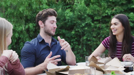 multi-cultural friends at home sitting at table enjoying food at summer garden party