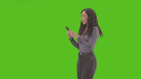 three quarter length portrait of woman text messaging on mobile phone against green screen