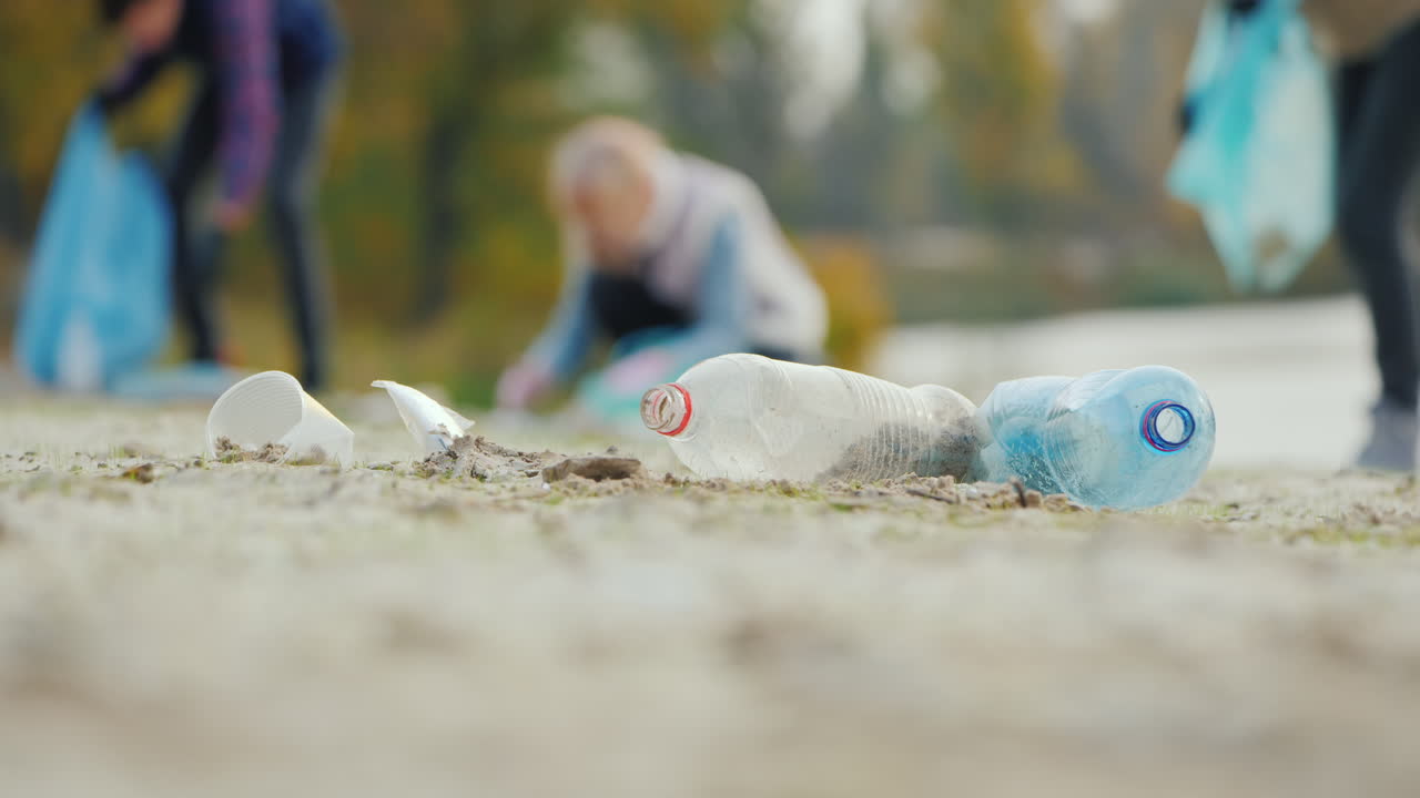 Rifiuti di plastica sulla spiaggia; sullo sfondo le persone stanno pulendo i rifiuti prendendosi cura dell'ambiente