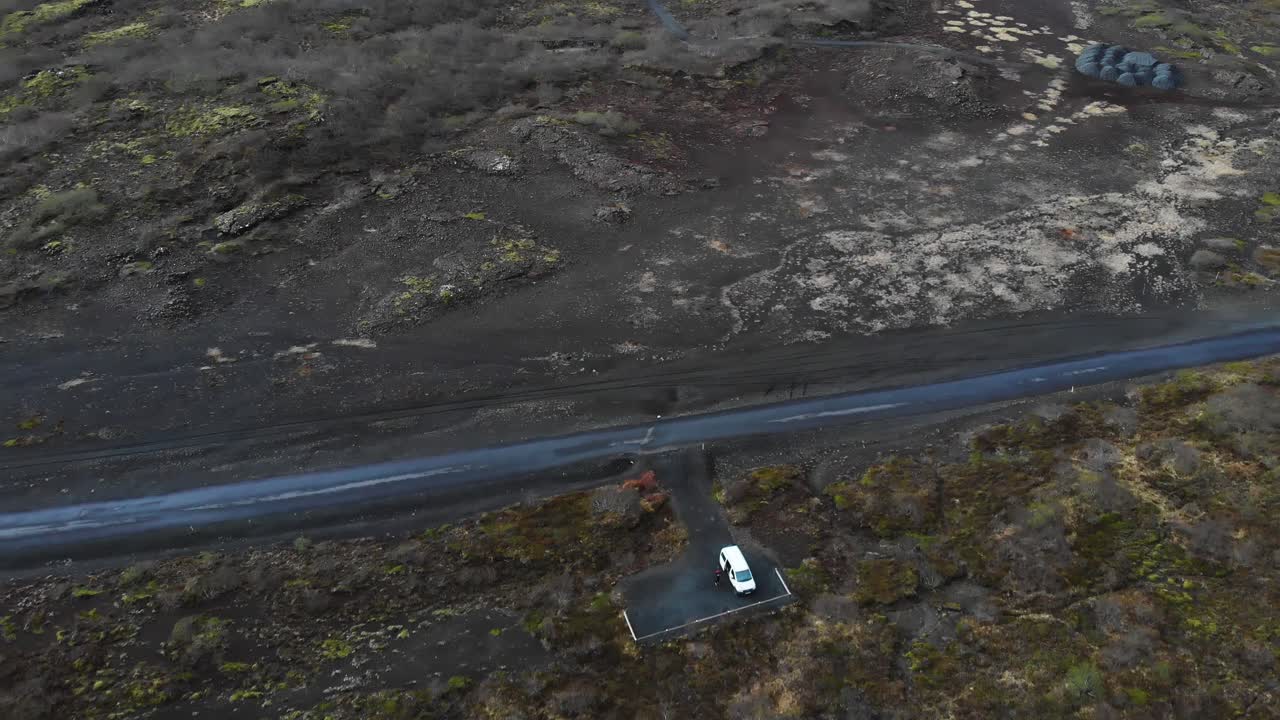 vista aérea sobre un camino de grava ubicado en las tierras altas de islandia que muestra el paisaje épico y una autocaravana acampada en un estacionamiento al costado del camino