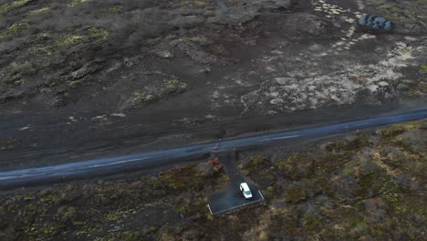 Vista-Aérea-Sobre-Un-Camino-De-Grava-Ubicado-En-Las-Tierras-Altas-De-Islandia-Que-Muestra-El-Paisaje-épico-Y-Una-Autocaravana-Acampada-En-Un-Estacionamiento-Al-Costado-Del-Camino