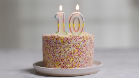 studio shot birthday cake covered with decorations and lit candle celebrating tenth birthday being blown out