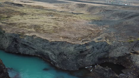 drone aerial view on deep volcanic canyon with clear turquoise glacial river and man on top of cliff above, unique landscape of icelandic highland