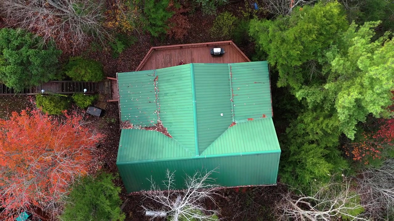 A 4K drone shot pointing downward as it circles upward, showcasing a cabin with a green roof nestled in the Smoky Mountains. The scenic view highlights its unique setting.