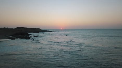 Aerial-forward-tilt-up-reveal-of-surfers-on-surfboards-waiting-for-wave-at-sunset